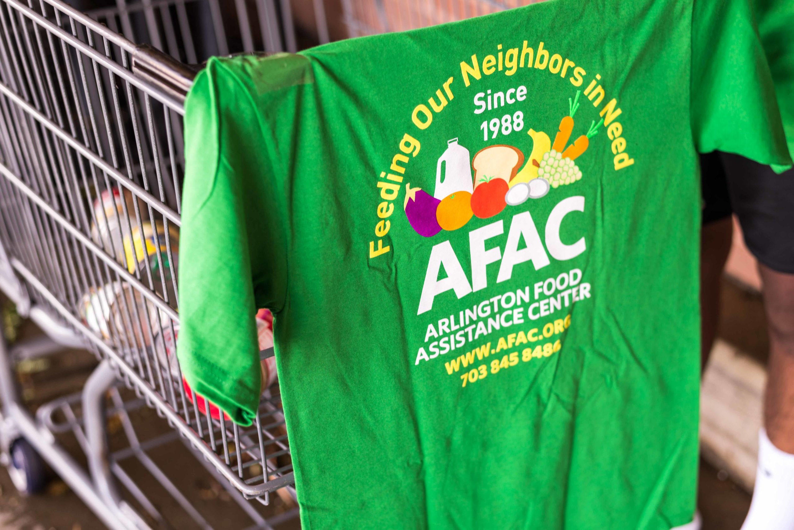 green T-shirt with AFAC logo hangs over shopping cart with food donations inside