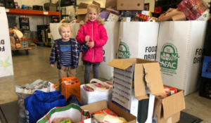 Two kids holding hands with food donations around them